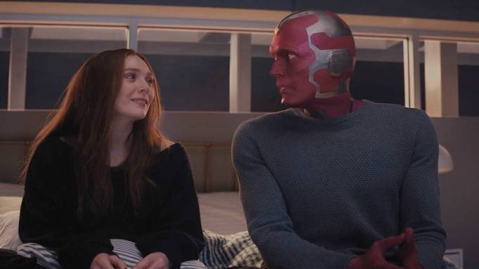Wanda Maximoff looks at Vision while sitting on a bed