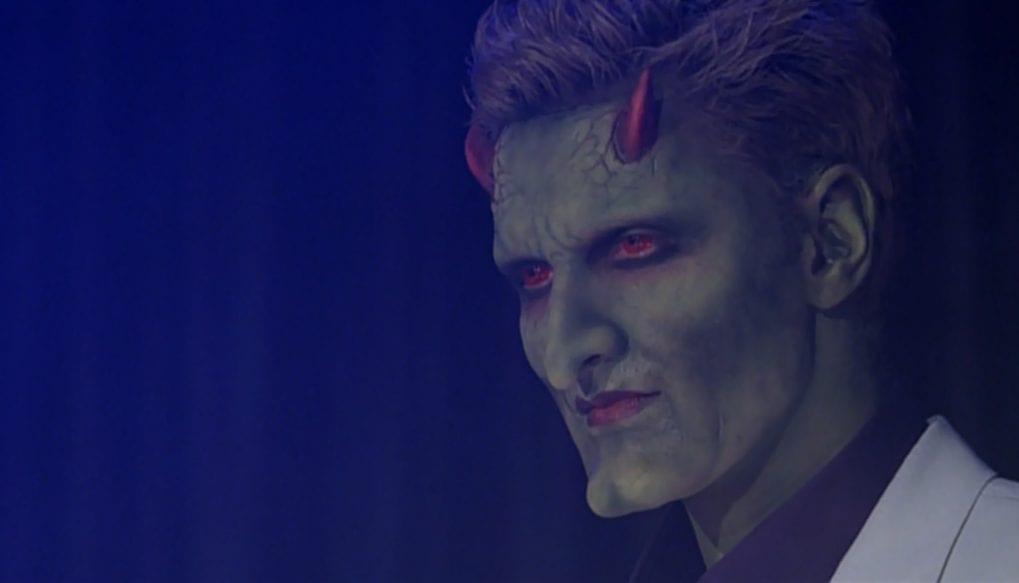 Lorne (green skin, little red horns, red eyes, snazzy suit) on stage in his first appearance in "Judgement"