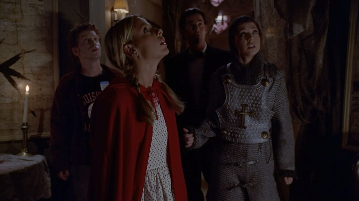 From left to right: Oz, Buffy, Xander, and Willow in their Halloween costumes looking up at the ceiling