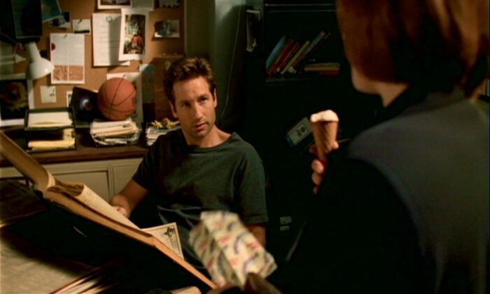 In the basement office, Mulder is reading old newspapers while Scully eats her tofutti dreamsicle