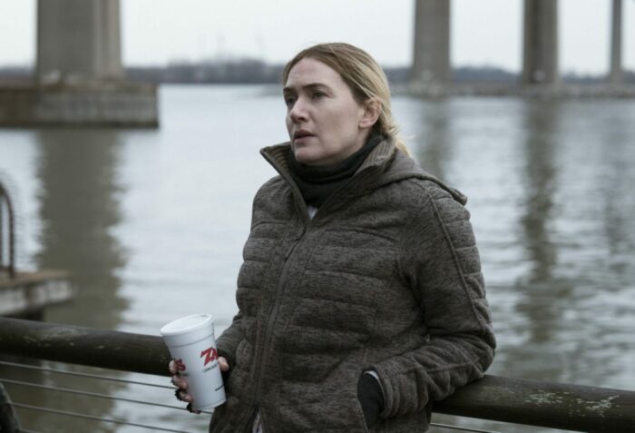 Mare (Kate Winselt) drinks coffee by a river.