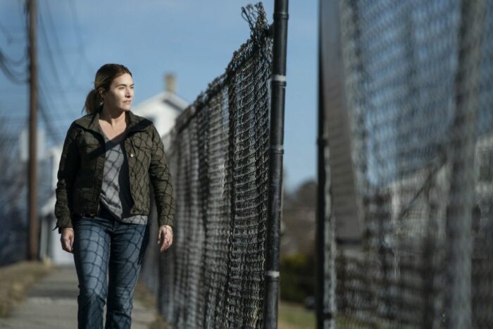 Mare (Kate Winslet) walks along a fence.