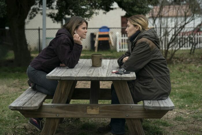 Carrie (Sosie Bacon) and Mare (Kate Winslet) attempt to have a civil conversation as they sit across from one another at a picnic table