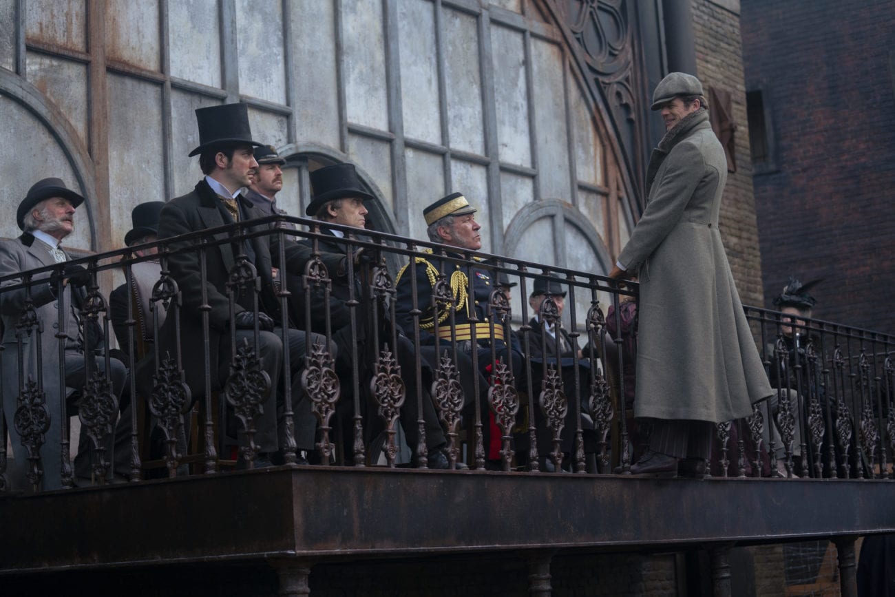 Hugo Swann stands on the outside of a balcony with Massen and other powerful men on the other side