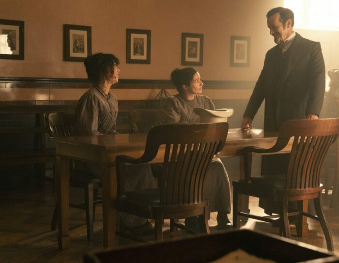 Sarah and Molly sit at a table in the asylum as Dr. Hague approaches them