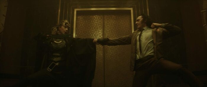 Loki and Sylvie end a fight in mirrored kneeling positions, holding each other's arms.