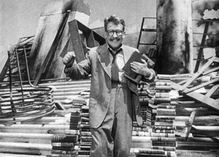 Still from The Twilight Zone episode "Time Enough at Last." Henry Bemis stands giddily on the steps of the ruined library surrounded by stacks of books.
