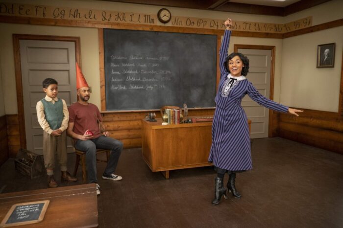 Miss Tate (Ariana DeBose) poses in front of a blackboard while Josh (Keegan-Michael Key) sits wearing a dunce cap and Carson (Liam Quiring-Nkind) looks on