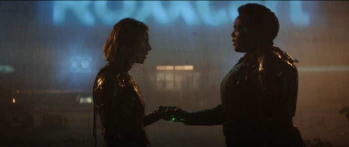 Sylvie (left) stands in the rain with Hunter B-15 (right), their hands glow with green light in the center.