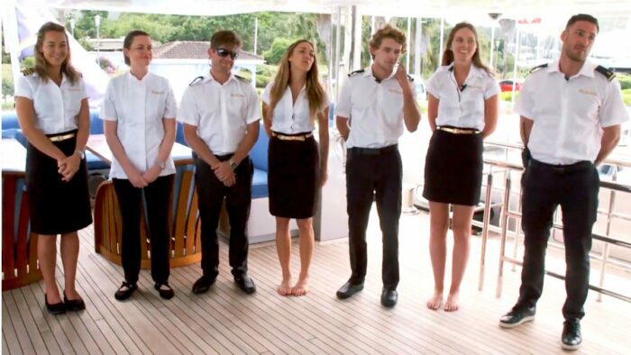 The cast of Below Deck stands in a line in uniform on a deck