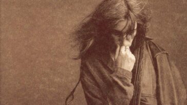 A sepia-tone album cover of the album Gone Again. Patti Smith stands in front of a blank wall with her hand down and her hand to her face.