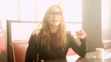 Tori Amos sits in a cafe booth wearing a black dress with her eyes closed in the Trouble's Lament music video