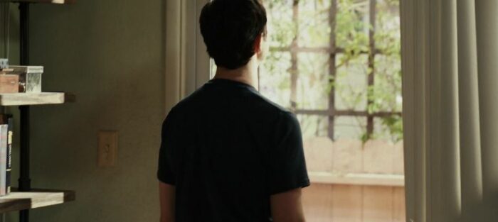 Josh stares out a window with his back to the camera