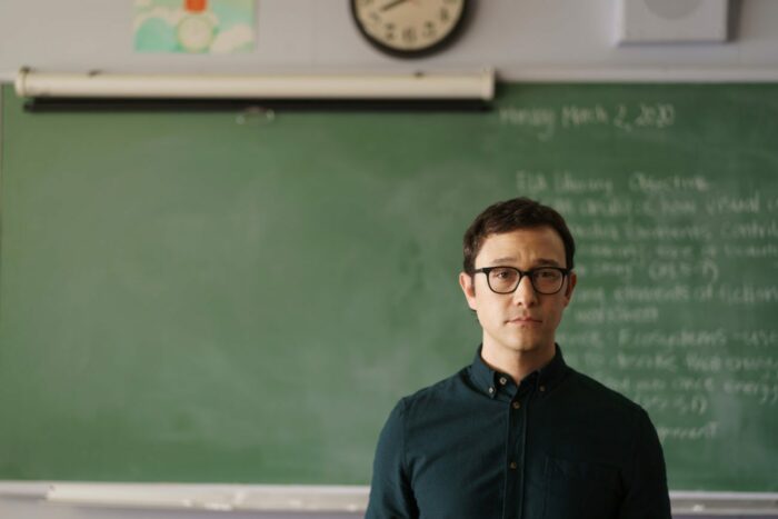 Josh Corman stands in front of a blackboard with Monday March 2, 2020 written at the top in Mr. Corman "Many Worlds"