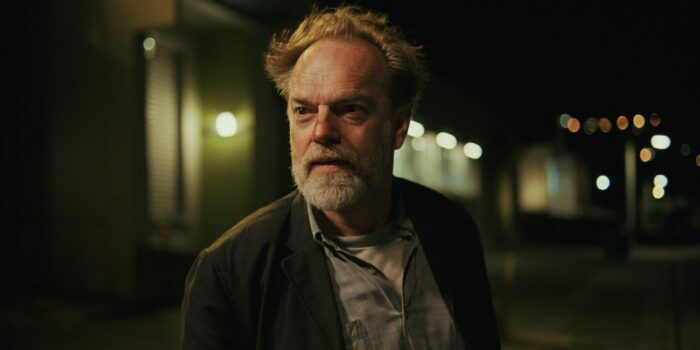 Hugo Weaving on the street with lights behind him in Mr. Corman