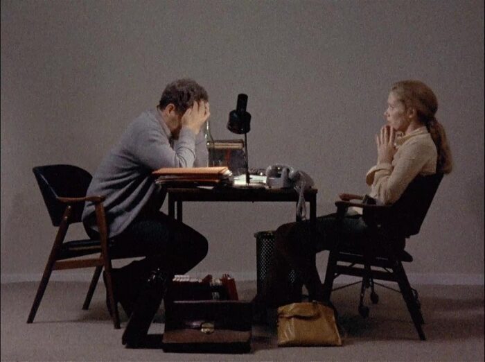 In this image from the 9173 Scenes from a Marriage, Johan (Erland Josephson) and Marianne (Liv Ullmann) are depicted facing each other over a small table, he with his head in his hands.