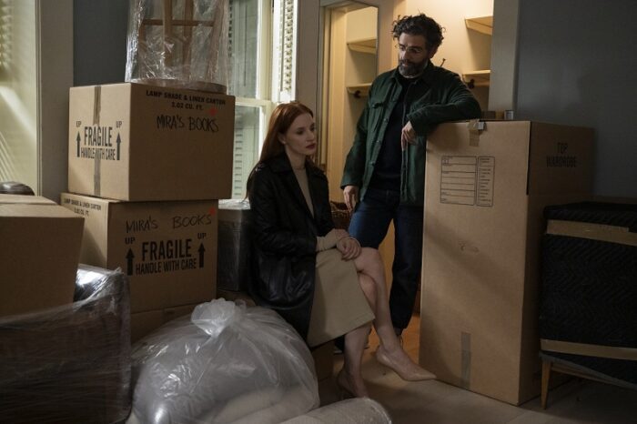 Mira (Jessica Chastain) sits and Jonathan (Oscar Isaac) stands, leaning on a packing box amid many in their house. a house full of packed boxes. 