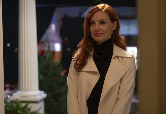 In this image from Scenes from a Marriage, Mira (Jessica Chastain) appears in a doorway wearing a black turtleneck and white coat.