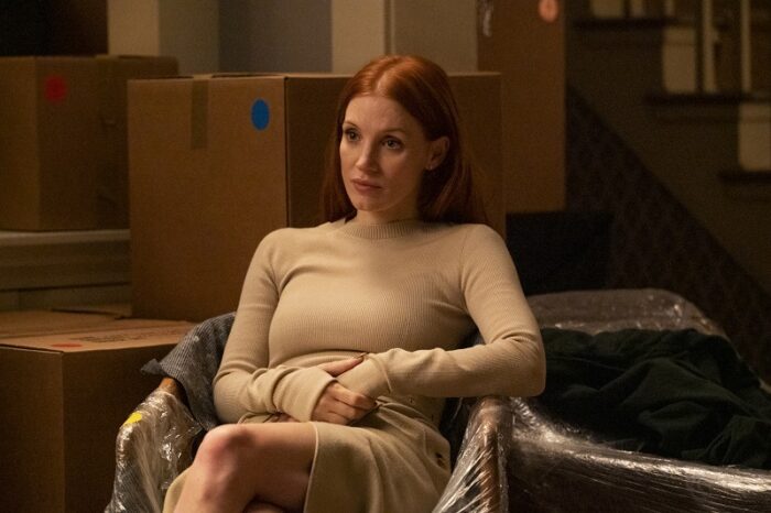 Mira (Jessica Chastain) sits on a wrapped sofa in front of packing boxes, looking pensively to her left.
