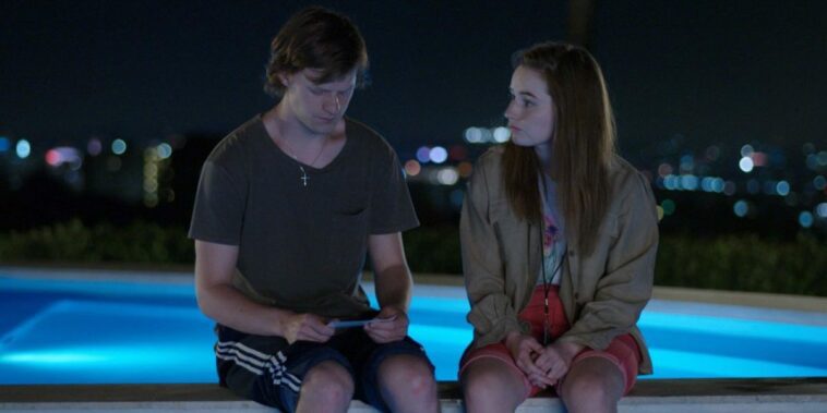 Abbi and Jesse Wheeler sit by a pool as he looks at a photo in his hands in The Premise S1E3
