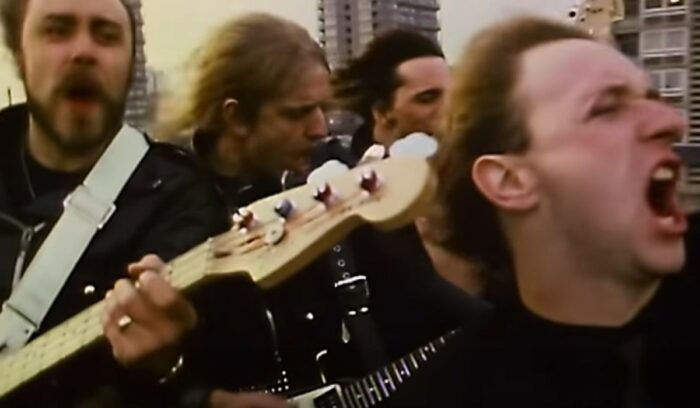 The heavy metal band Judas Priest in a car, singing and playing down a highway