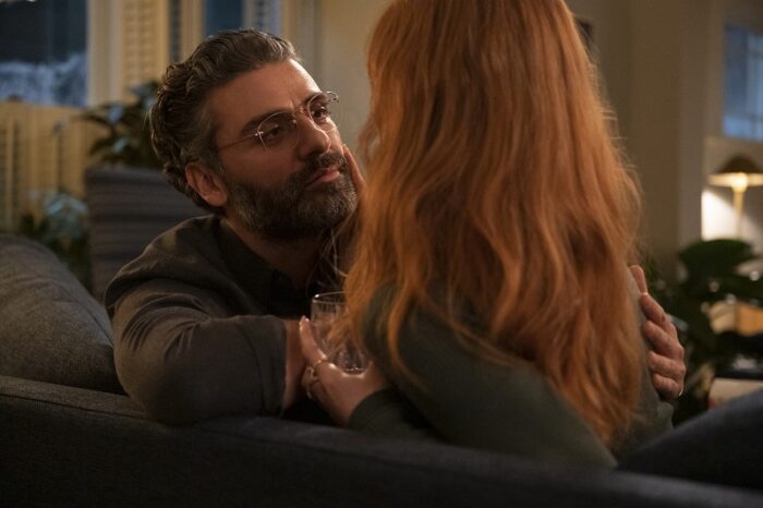 In this image from Scenes from a Marriage Episode 5, Mira (Jessica Chastain, her back to the camera) and Jonathan (Oscar Isaac) sit together on the sofa in their former home as Mira strokes Jonathan's beard.