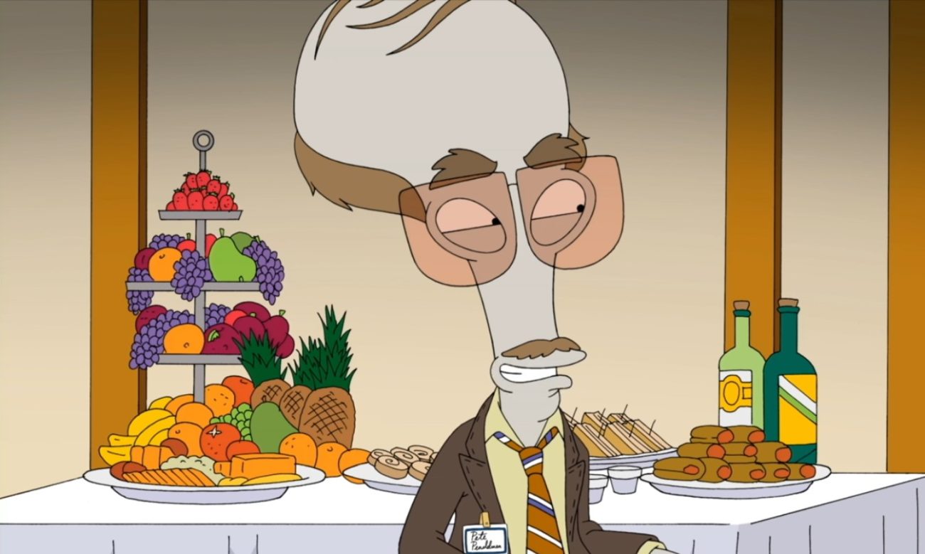 A grey bulbous-headed alien wears tinted pink reading glasses and a suit and tie; he stands in front of a serving table covered in fruits and vegetables (Roger Smith as Pete Pendelman in American Dad!)