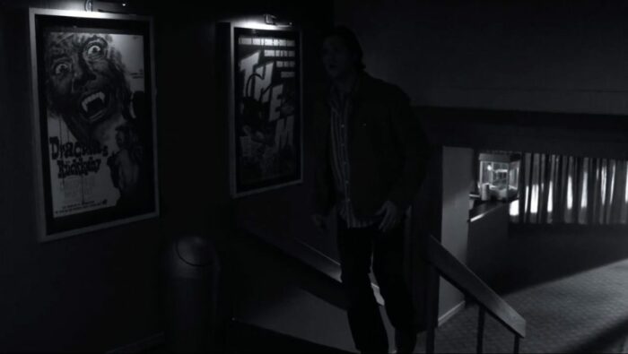 Sam Winchester walking into an old-fashioned theatre with posters of Them! and Dracula Has Risen From the Grave on the wall