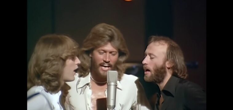 The Bee Gees gather around one microphone to sing