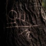 A stick figure drawing carved into the bark of a tree