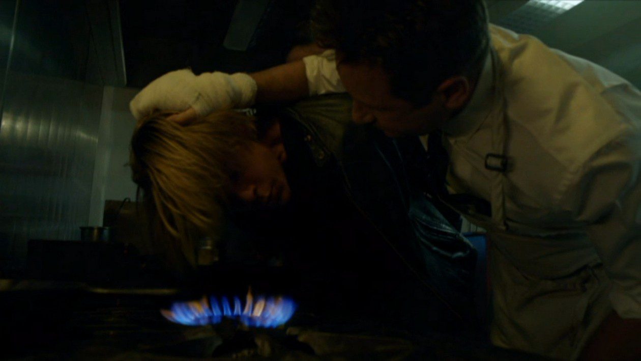 Sam Hodiak holds a man's face over the flame on a gas cooker