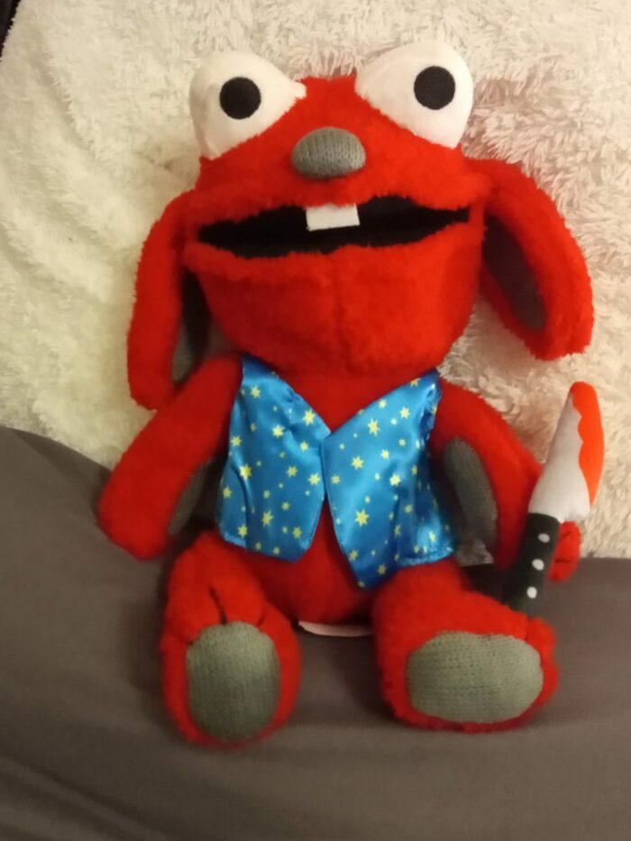 A red Benny plush toy rests against a pillow