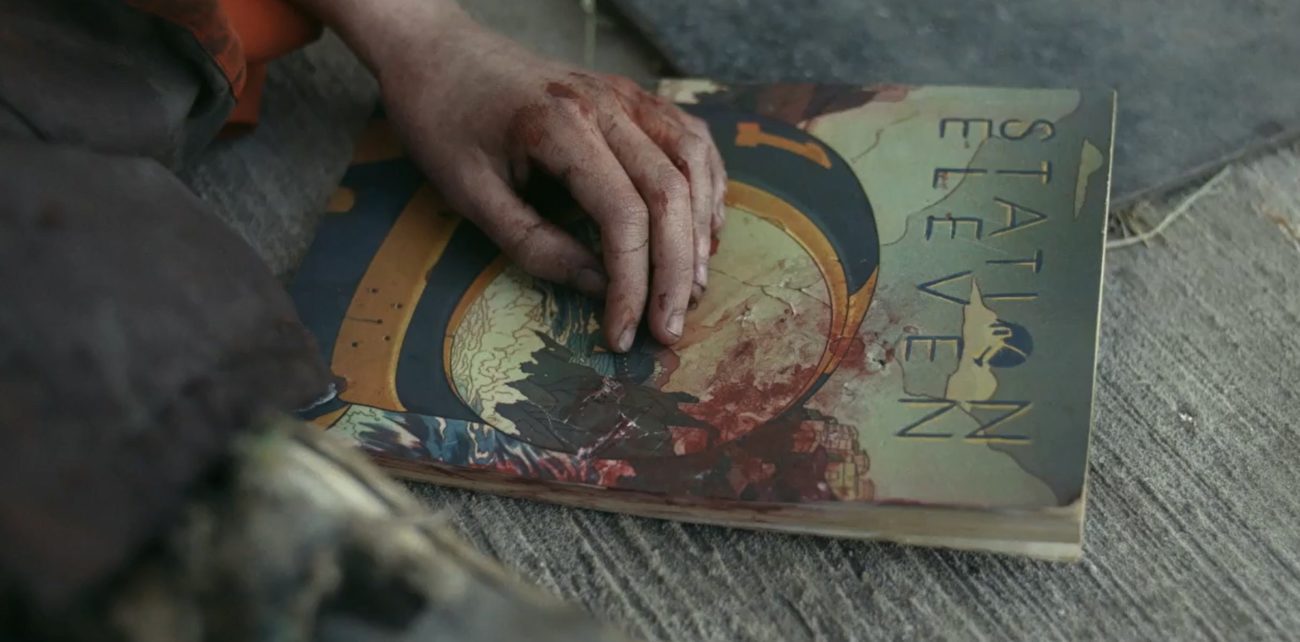 A hand resting on a battered and bloody copy of the Station Eleven graphic novel