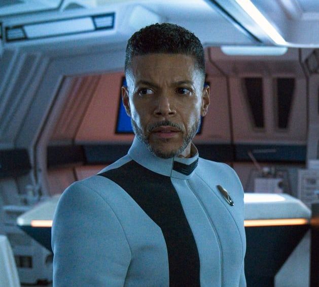 Dr. Culber (Wilson Cruz) stands and looks dramatically toward the side