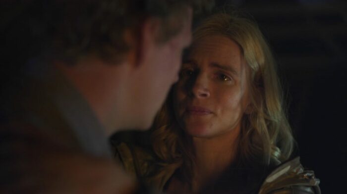 OA (Brit Marling) looking tenderly at Steve (Patrick Gibson) in a dark room.
