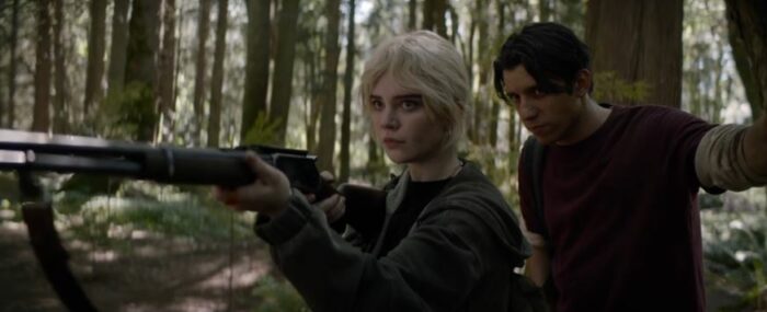 Young Natalie points a rifle in the woods, with Travis looking over her shoulder