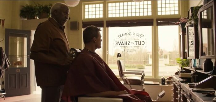 Jack Reacher sits in a barbers chair and he gets a haircut, he looks out the window, and the barber stands behind him talking to the man. 