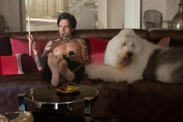 Tommy (Sebastian Stan) twirls his drumstick while sitting on the couch with his dog.