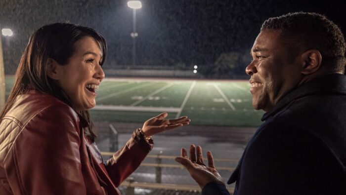 Zoe (Zoe Chao) and Aniq (Sam Richardson) look at each other in front of a football field in the rain