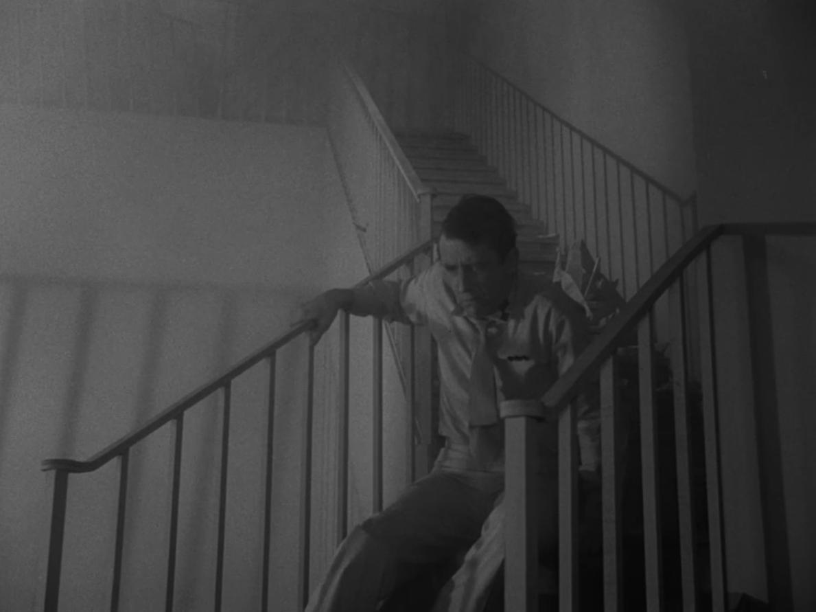 A man sits in the middle of a flight of stairs, holding on to the bannister.