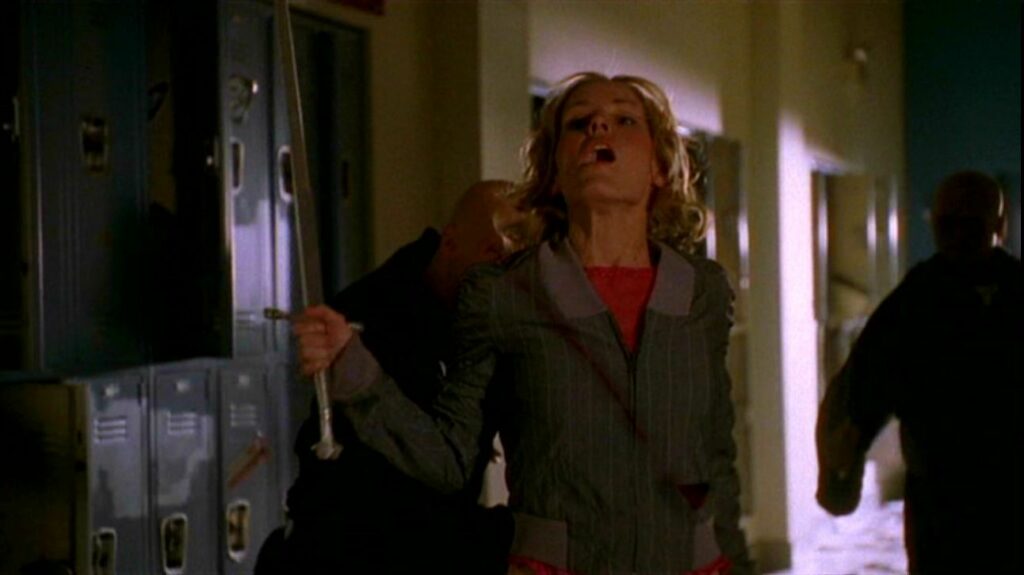 Anya Jenkins (Emma Caulfield), holding a sword in her right hand and gasping in surprise, is sliced in half by a black-robed minion behind her.