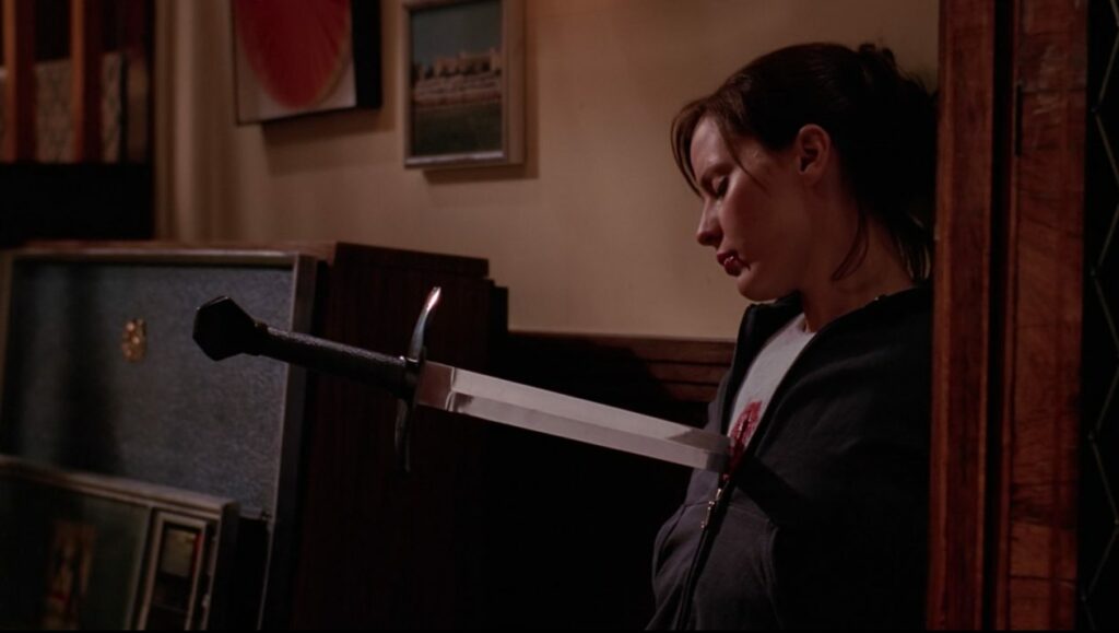 Anyanka (Emma Caulfield), blood pouring from her mouth and chest, is pinned to the wall by a sword through her chest.