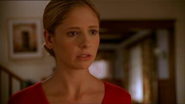 Buffy Summers (Sarah Michelle Gellar) stands alone in her living room and stares forward in shock.