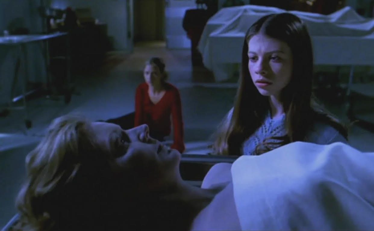 As Buffy Summers (Sarah Michelle Gellar) sits exhausted on a white morgue floor, Dawn Summers (Michelle Trachtenberg) stares confused at the corpse of her mother Joyce Summers (Kristine Sutherland), who is covered up to the neck by a sheet on an embalming table.