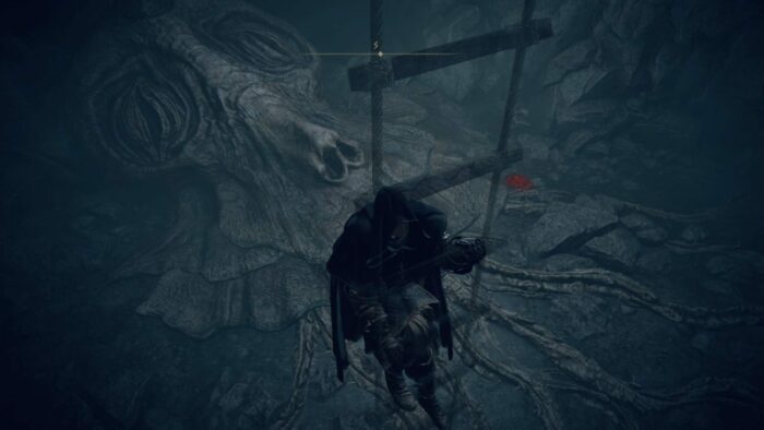 A dark figure on a ladder above a scary face on the ground below in Elden Ring