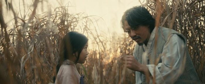 Sunja as a child and her father, in a field, as he leans towards her