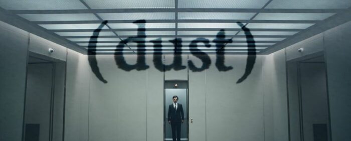 Mark stands in the elevator with the word "dust" appearing on screen above him in parentheses