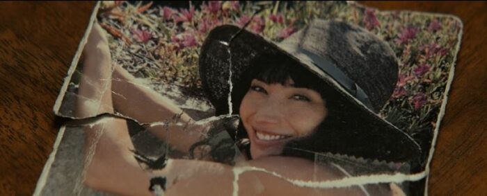 A torn photo, taped back together, shows Dichen Lachman smiling and wearing a hat