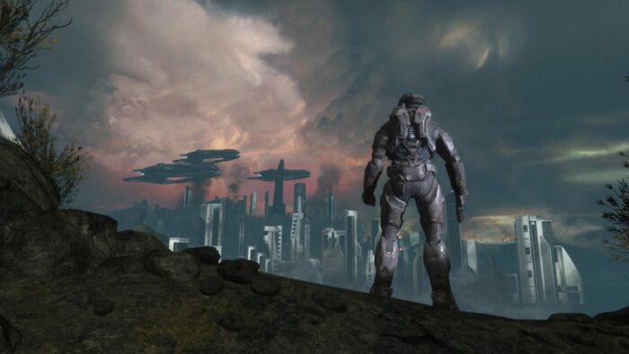 Noble 6, atop a large hill, gazes out at a city besieged by the Covenant in the distance.