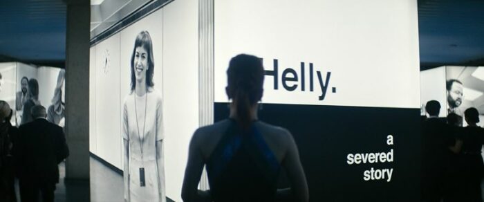 Helly looks at a cube, with a picture of herself on one side and on another the words "Helly. a severed story"
